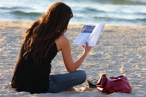Woman Reading Book In Her Hand And Sitting On The Beach