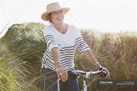 Smiling Mature Woman Riding Bicycle On Sunny Beach Grass Path Healthy Living Mode Of