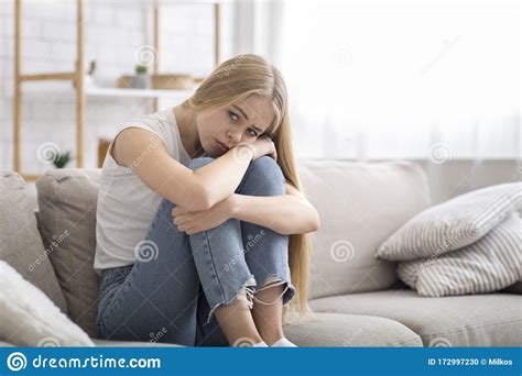 Lonely Sad Girl Sitting On Couch At Home Alone Stock Photo