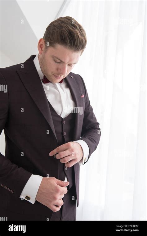 Side View Of Young Handsome Man Standing In White Bedroom And Putting
