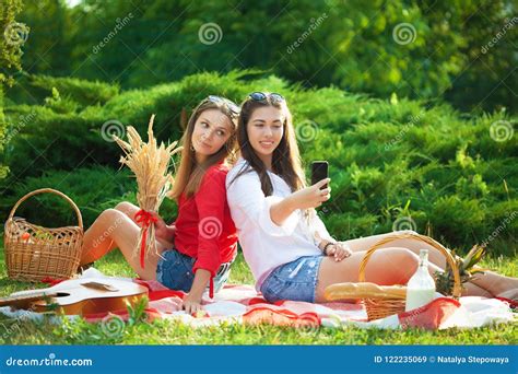 Two Young Beautiful Girls Having Fun On The Picnic Making Selfie On A Smartphone Stock Image