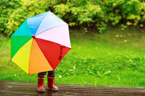 Little Kid Is Playing In The Rain With A Colorful Umbrella