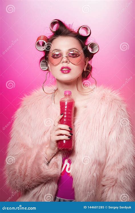 happy girl with bottle and pink water posing on pink background in body and fur coat with