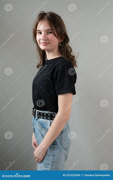 Portrait Of A Shy Brunette Teen Girl In Black T Shirt On Gray