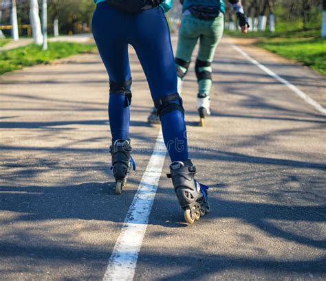 Two Girls On Roller Skates Ride Along The Road Next To Each Other Stock