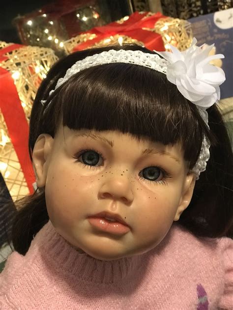 A Close Up Of A Doll Wearing A Pink Sweater And White Flower In Her Hair
