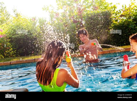 group of three teens play with water gun squirt pistol on swimming pool outside on sunny day