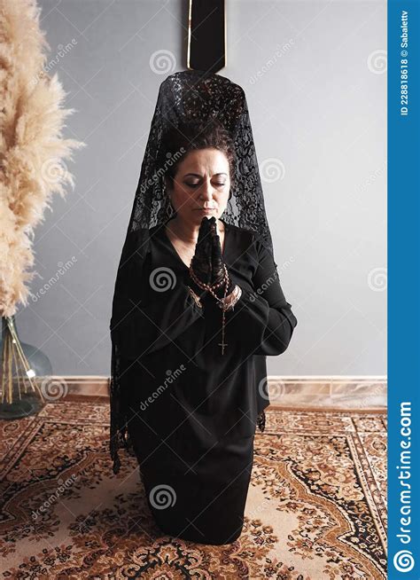 Woman On Her Knees With A Veil And A Black Suit Praying With A Rosary