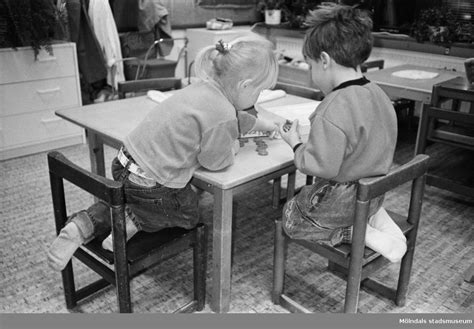 en flicka och en pojke fotograferade bakifrån sitter vid ett lågt bord och pysslar i