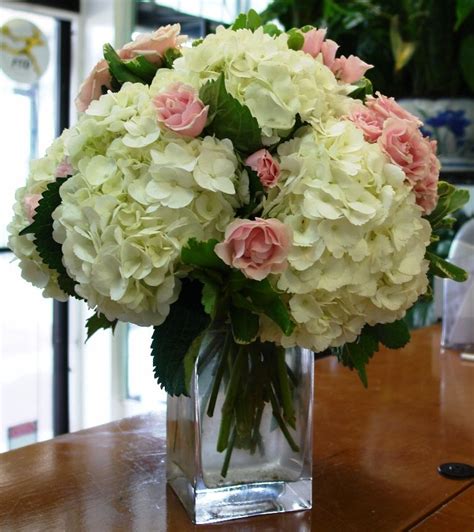 low centerpiece of white hydrangeas pink roses and pink spray roses in a vase with exposed