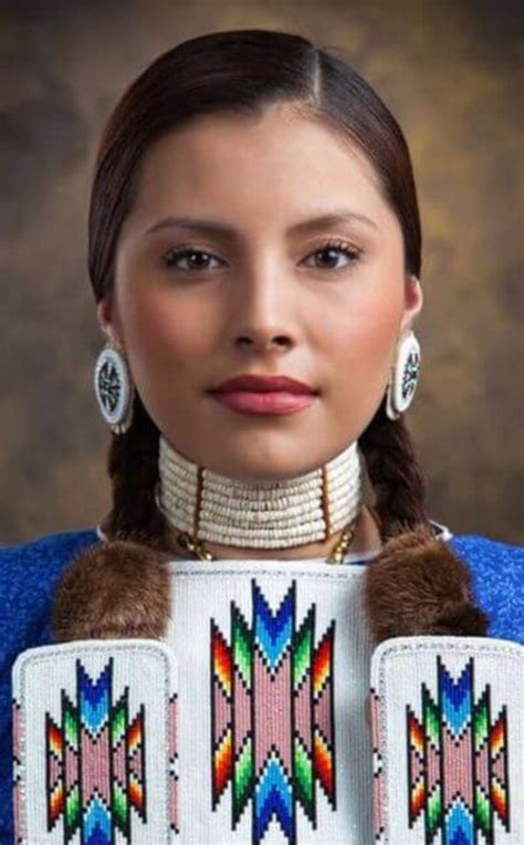 a woman with braids and earrings on her head wearing a blue sweater and white shirt