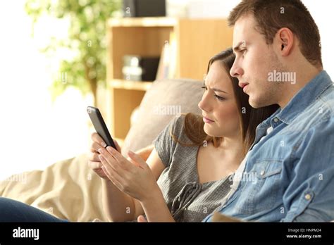 Upset Couple Checking Content In A Phone Sitting On A Sofa In The