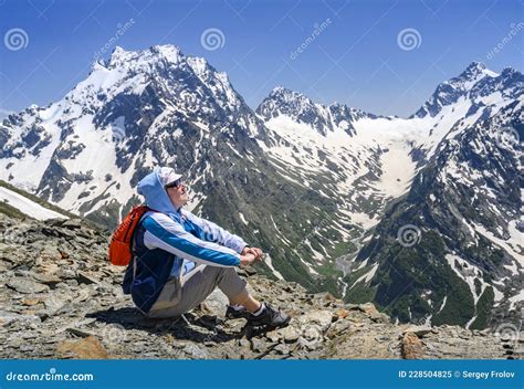 A Tourist High In The Dombay Mountains Covered With Snow Admires The