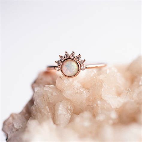 An Opal And Diamond Ring Sitting On Top Of A Rock In Front Of A White