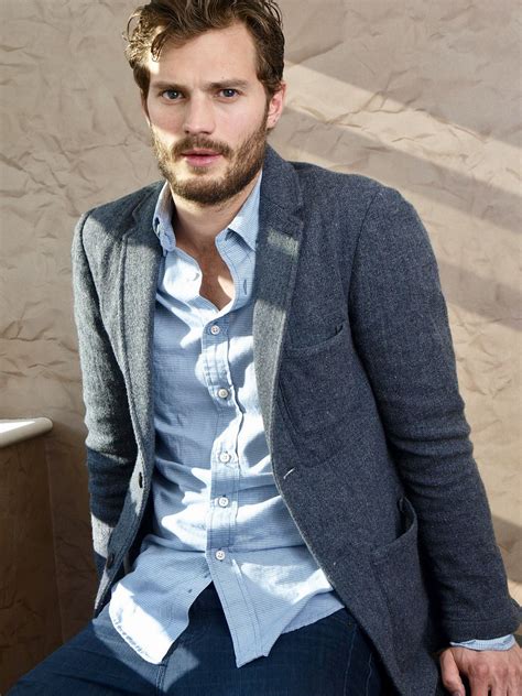 A Man Sitting Down Wearing A Suit And Tie With His Hands In His Pockets Looking At The Camera