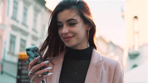 Happy Young Woman Uses Phone Stand In The City Center Looks Around