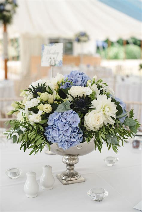 An Elegant Arrangement Of Pale Blue And Ivory Flowers For These Table