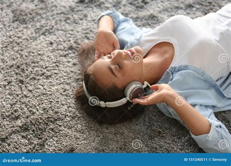Beautiful Young Woman Listening To Music While Lying On Carpet At Home