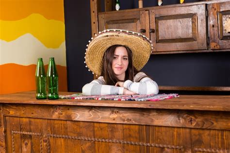 Una Mujer Joven Con Un Sombrero Se Inclinó Sobre La Barra De Bar Con Botellas De Cerveza En El