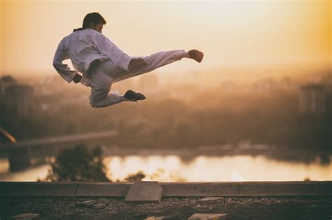 Skillful Martial Artist Performing Fly Kick At Sunset Stock Photo