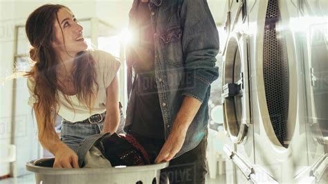 Couple In A Laundry Room Washing Clothes With Sun Flare In The Background Man And Woman Putting