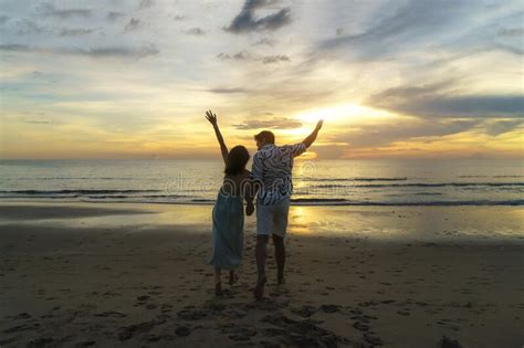 Asian Couple Jumping On The Beach Near Sea With Beautiful Sunset