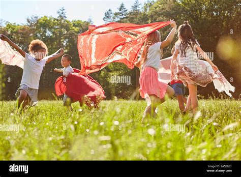 Group Of Kids Runs And Dances With Towels On A Meadow In Summer Stock