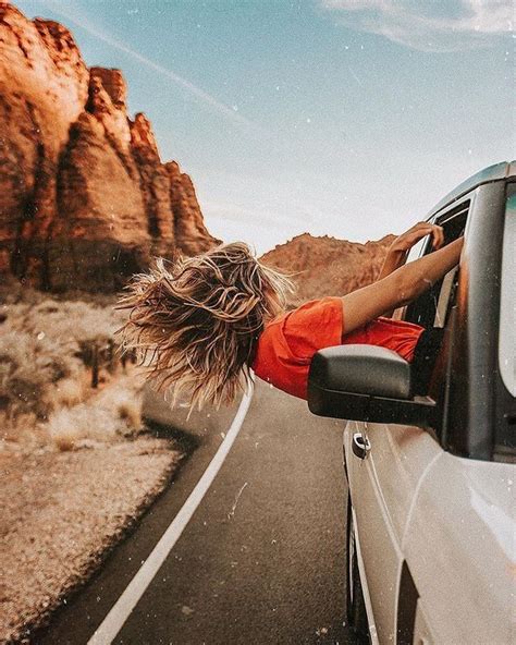 A Woman Leaning Out The Window Of A Car On A Desert Road With Mountains