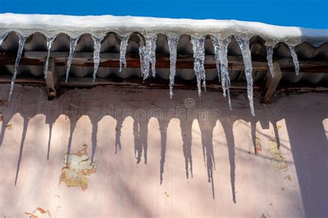 Long Icicles Hang From The Snow Covered Roof Of An Old Pink House