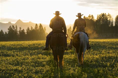 Two Cowboys Riding On Horseback In A Prairie Landscape At Sunset Stock