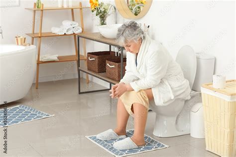 Elderly Woman With Hemorrhoids Sitting On Toilet Bowl In Bathroom Foto