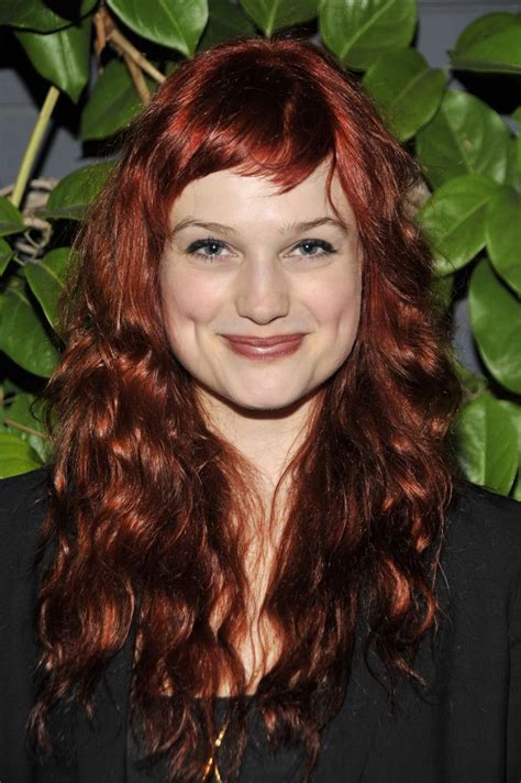 A Woman With Red Hair And Blue Eyes Smiles At The Camera While Standing