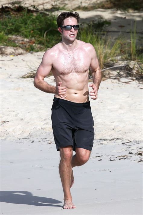 Man wearing in blue swimming trunks and shows by his right hand to right side. Robert Pattinson Working Out Shirtless on the Beach—Pics