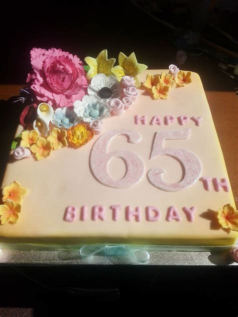 A Birthday Cake With White Frosting And Flowers On It That Says Happy 65th