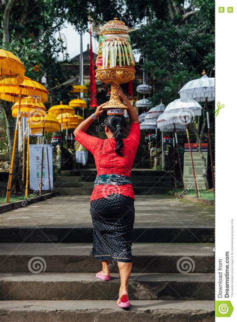 Balinese Woman In Traditional Clothes Carrying Ceremonial Offerings On