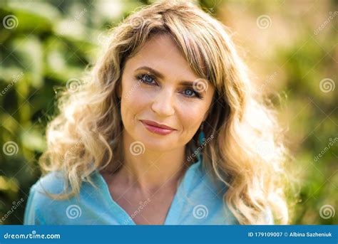 close up portrait of beautiful smiling blonde 40 years old woman in blue shirt looking in camera