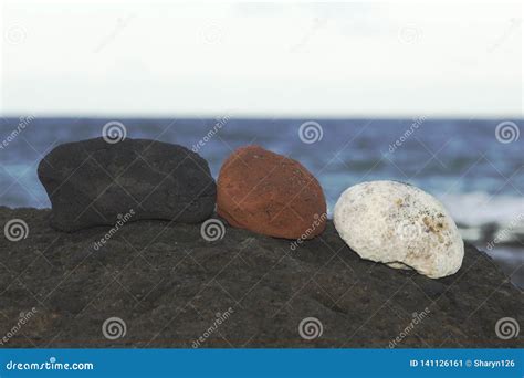 Three Different Coloured Rocks On A Black Rock In Front Of The Ocean