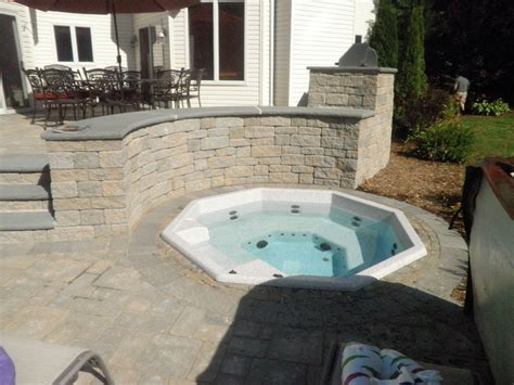 In Ground Hot Tub Surrounded By Paver Patio And Stone Wall Along Side Outdoor Kitchen All