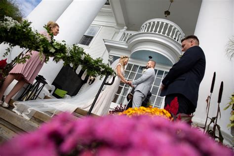 A Bride And Groom Standing In Front Of A White House With Pink Flowers
