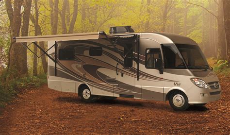 An Rv Is Parked In The Woods With Its Awning Open And Trees Around It