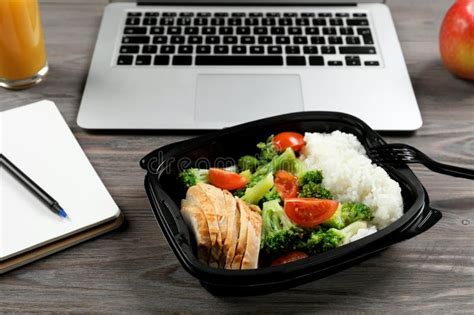 Container With Tasty Food Notebook And Laptop On Wooden Table