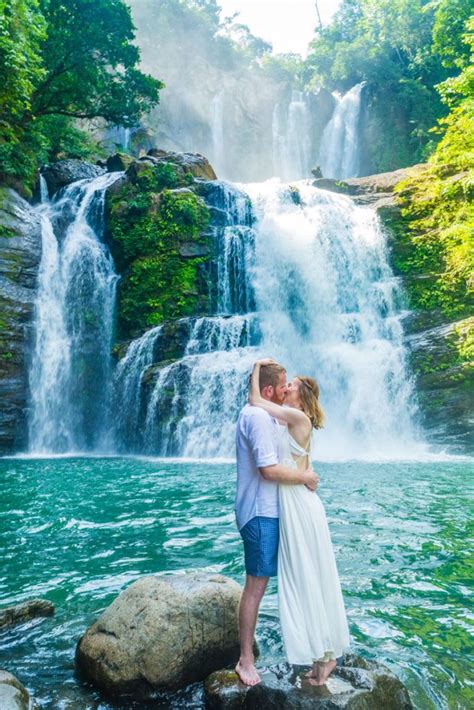 A Couple Kissing In Front Of A Waterfall