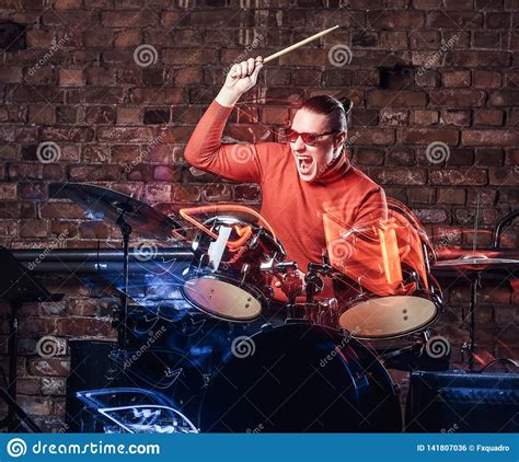 Stylish Musician In Sunglasses Emotionally Playing Drums Against Brick Wall Background Stock