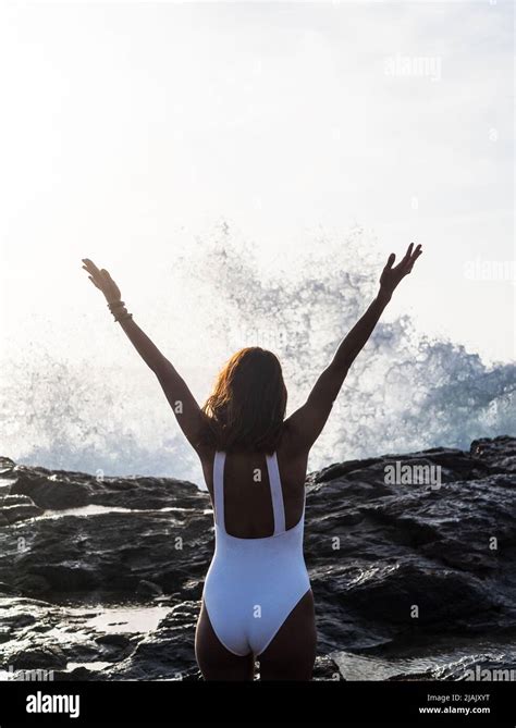 Woman From Behind By The Sea With Arms Raised When A Wave Breaks