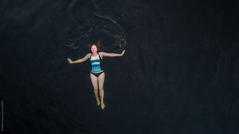 aerial photo of woman swimming peacefully in dark freshwater cottage lake by stocksy