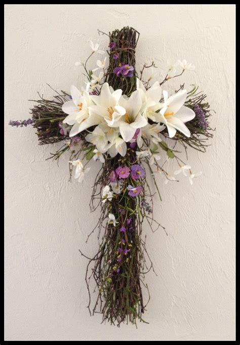 A Cross Made Out Of Branches And Flowers Hanging On The Side Of A White