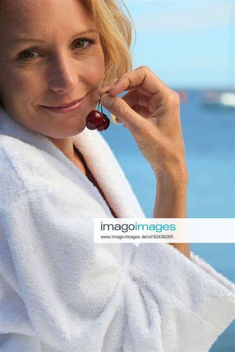 50 years old blonde woman dressed in bathrobe in front of the sea taking cherries in her fingers mod