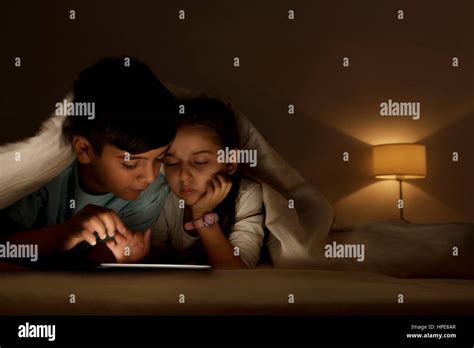 Brother And Sister Using Digital Tablet Lying In Bed Under The Covers