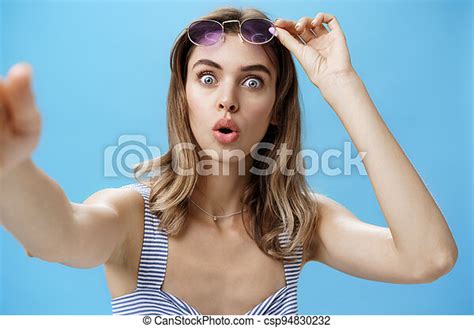 woman taking off glasses while looking at herself in frontal camera of smartphone holding