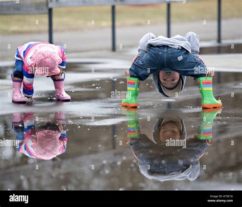 Two Small Children Playing In Puddle Looking At Reflections In Water